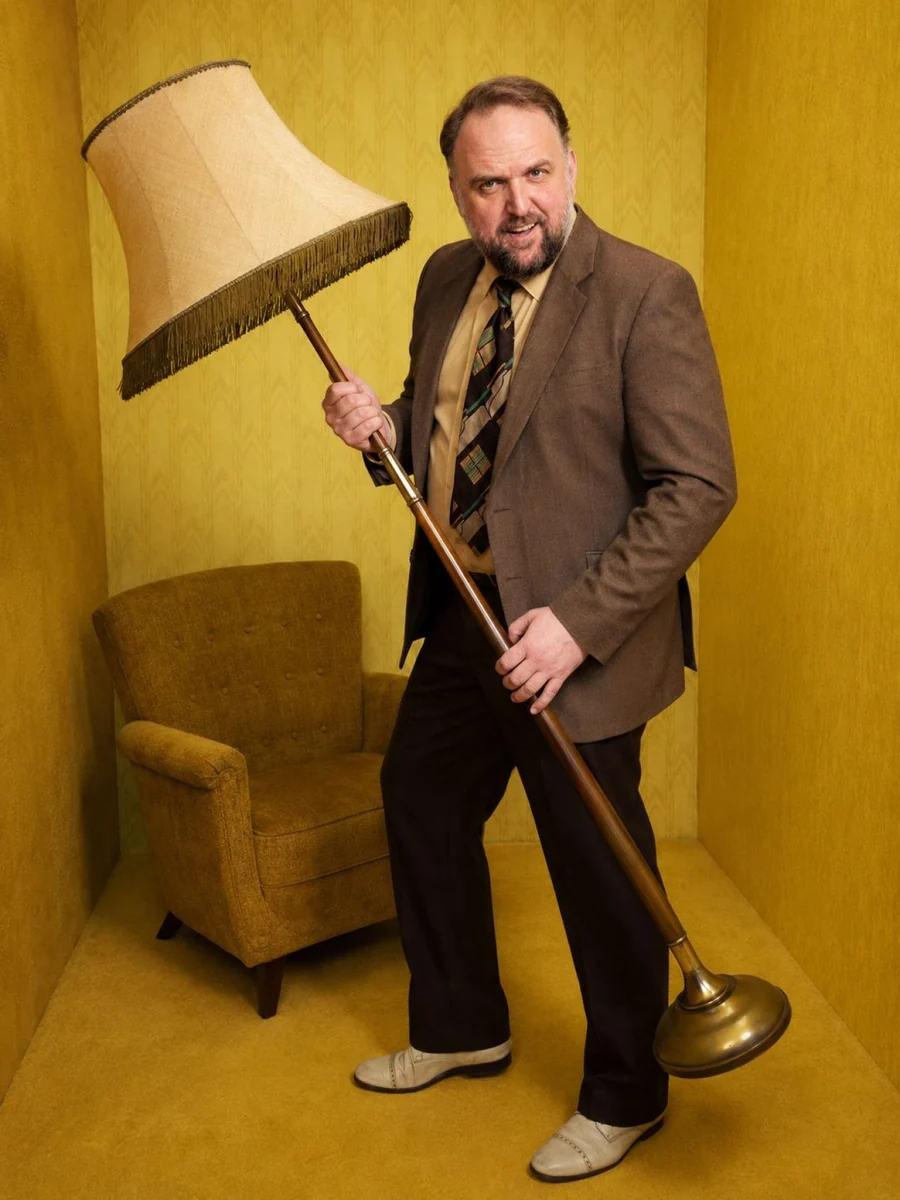Ganzkörperaufnahme von Ronny Schuster im braunen Anzug mit Stehlampe.
