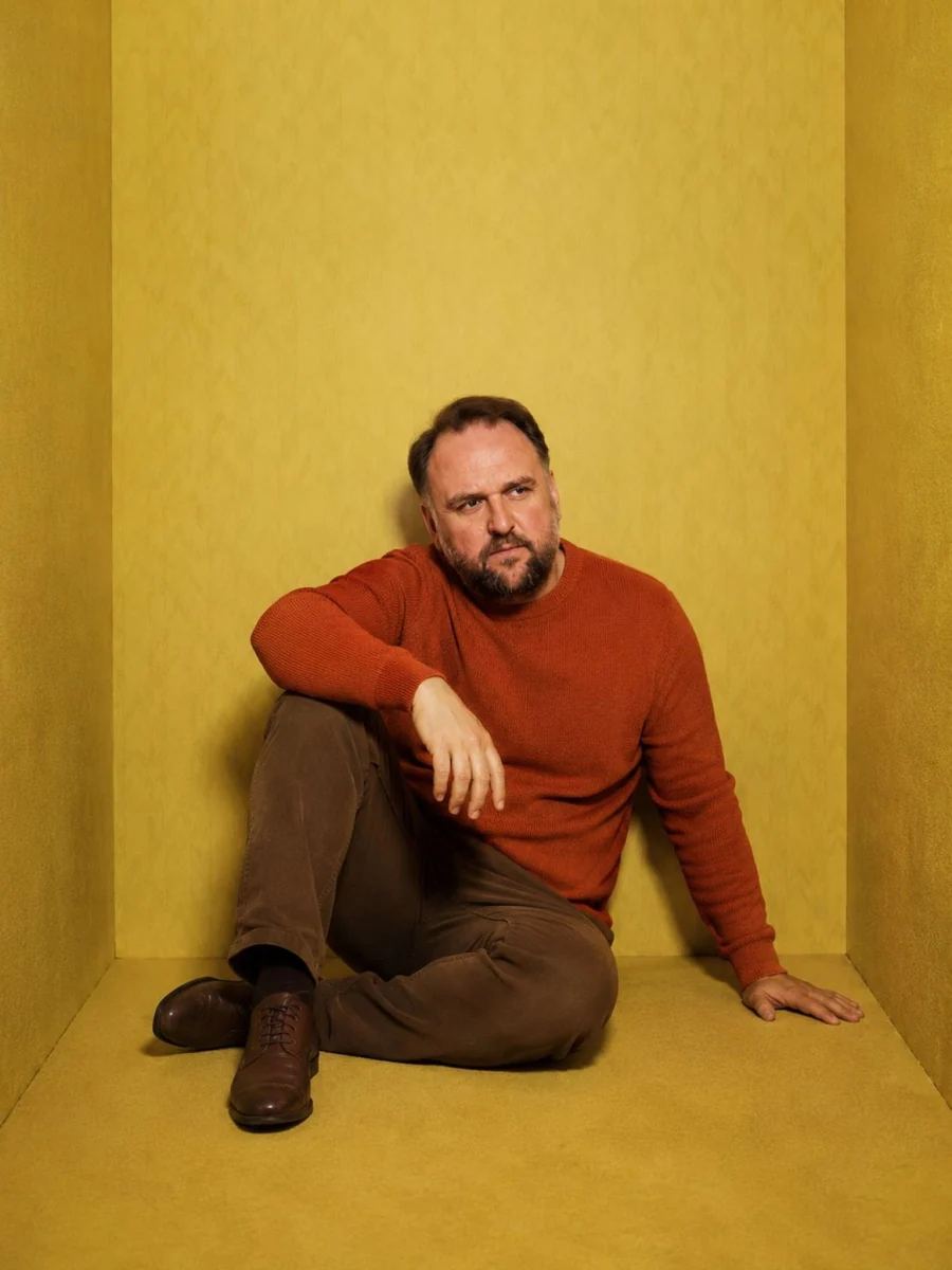Ronny Schuster sitzt in rostfarbenem Pullover auf dem Boden.