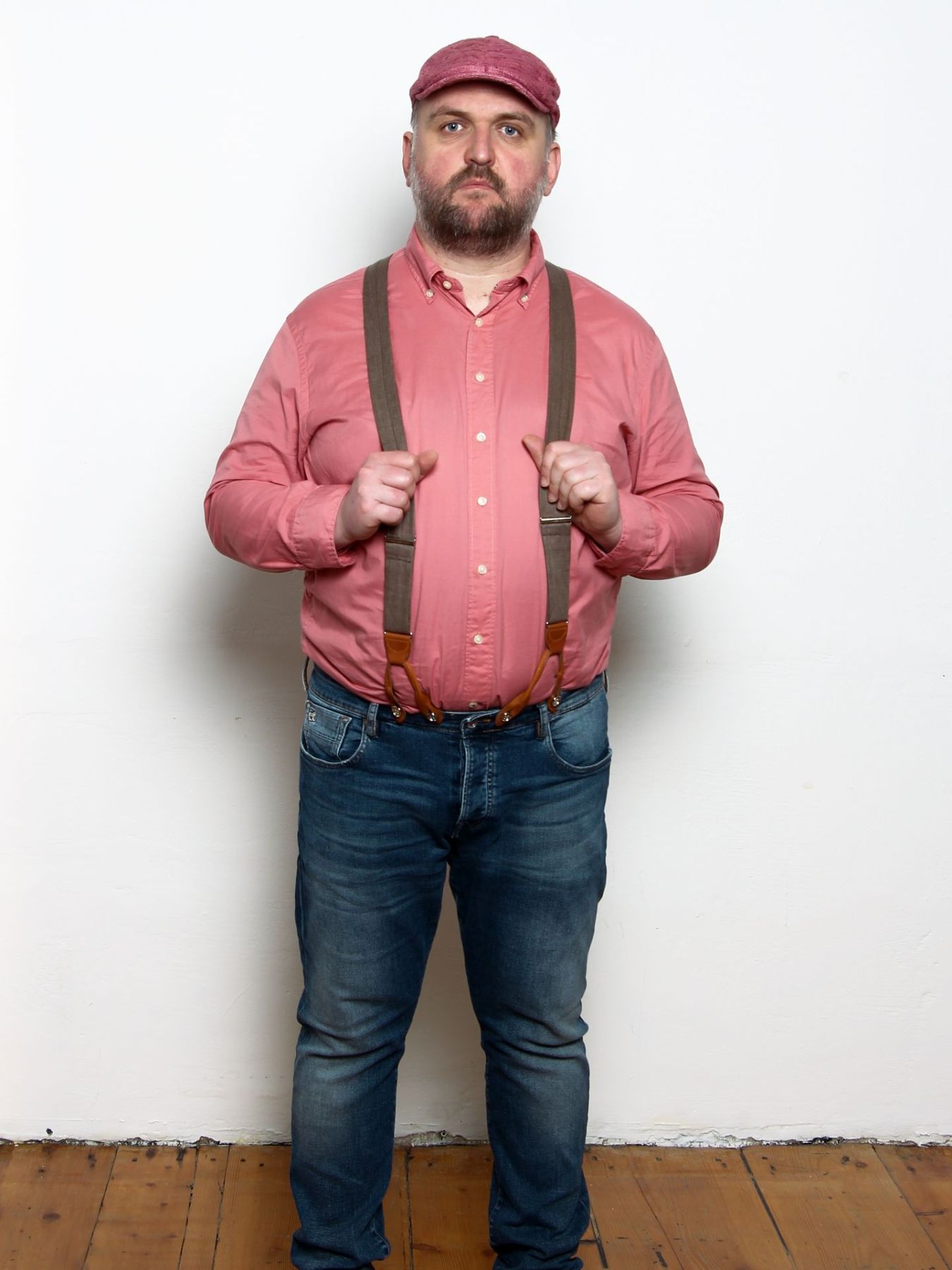 Ronny Schuster steht in rotem Hemd, Jeans, Hosenträgern und roter Schiebermütze.