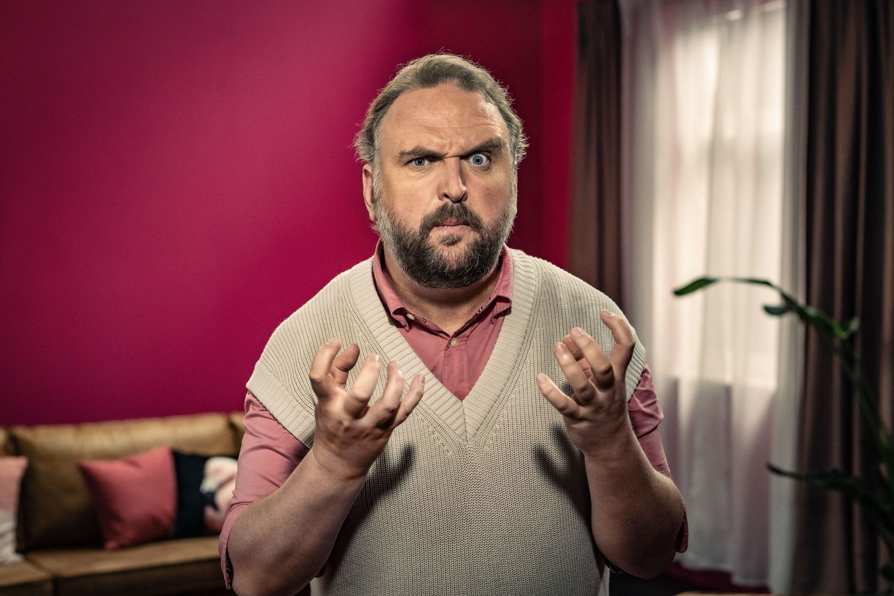 Ronny Schuster im hellen Pullunder und rosa Hemd mit fragend erhobenen Händen.