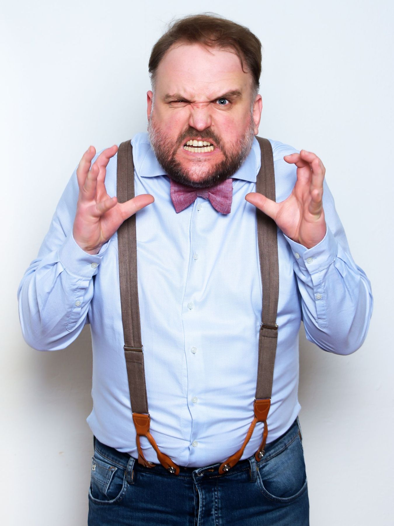 Ronny Schuster in blauem Hemd, Fliege und Hosenträgern mit überzeichneter Mimik.