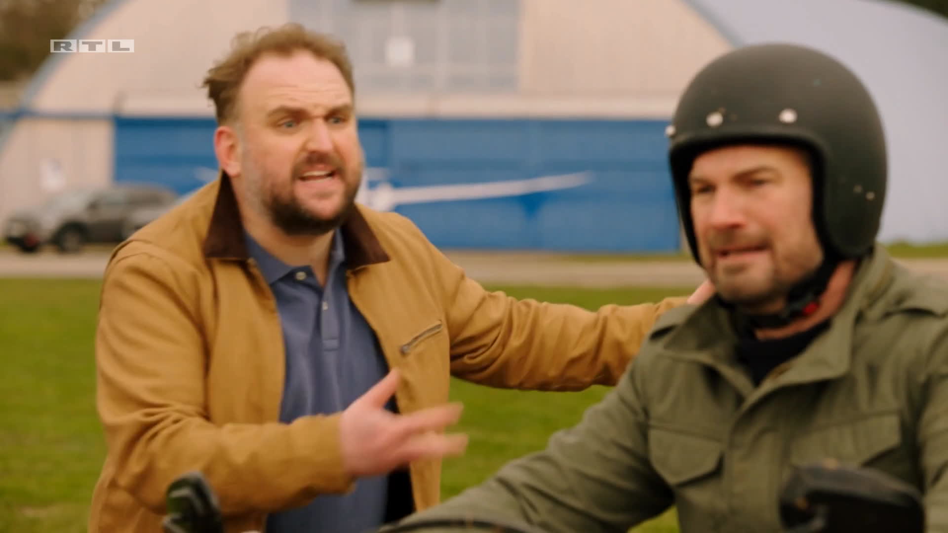 Ronny Schuster in brauner Jacke neben einem Mann mit Motorradhelm.