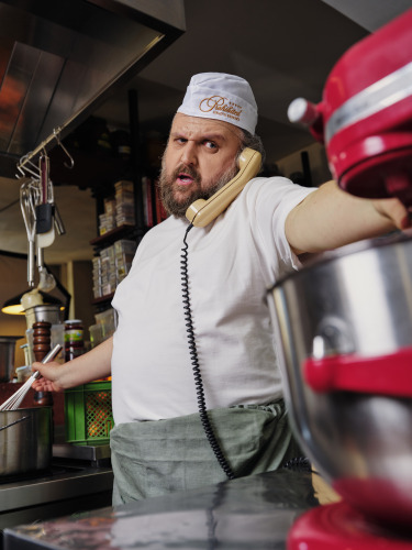 Ronny Schuster mit weißer Kochmütze und Telefonhörer in einer Restaurantküche.