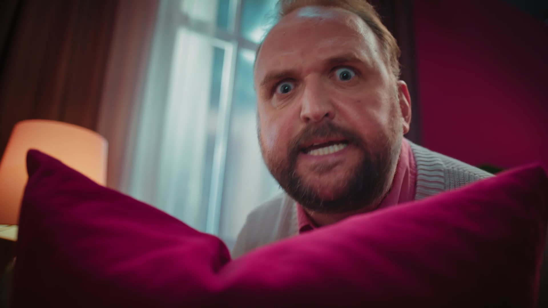 Ronny Schuster blickt über ein kräftig pinkfarbenes Sofakissen.