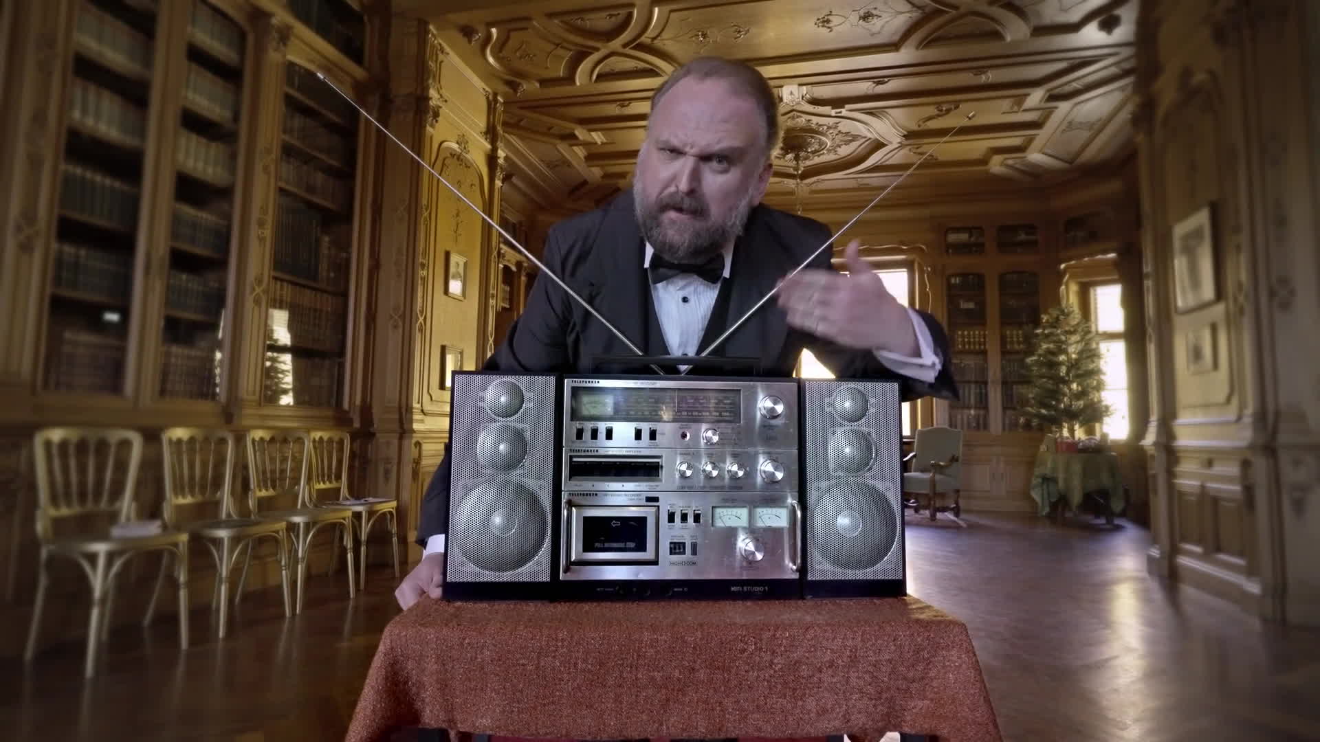 Ronny Schuster als Butler hinter einem Radiorecorder in einem historischen Saal.