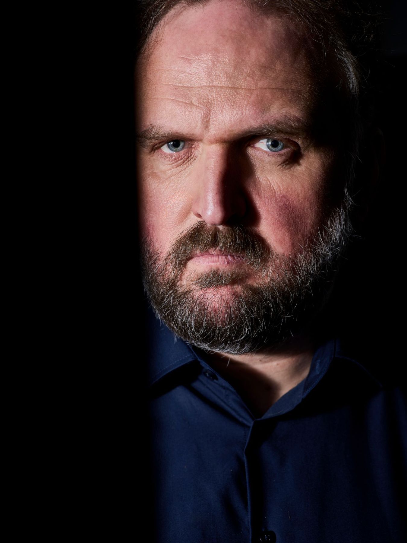 Nahporträt von Ronny Schuster im dunkelblauen Hemd mit ernstem Blick.