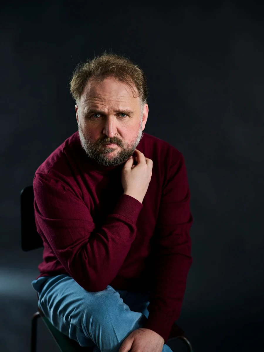 Ronny Schuster sitzt in burgunderfarbenem Pullover und Jeans.