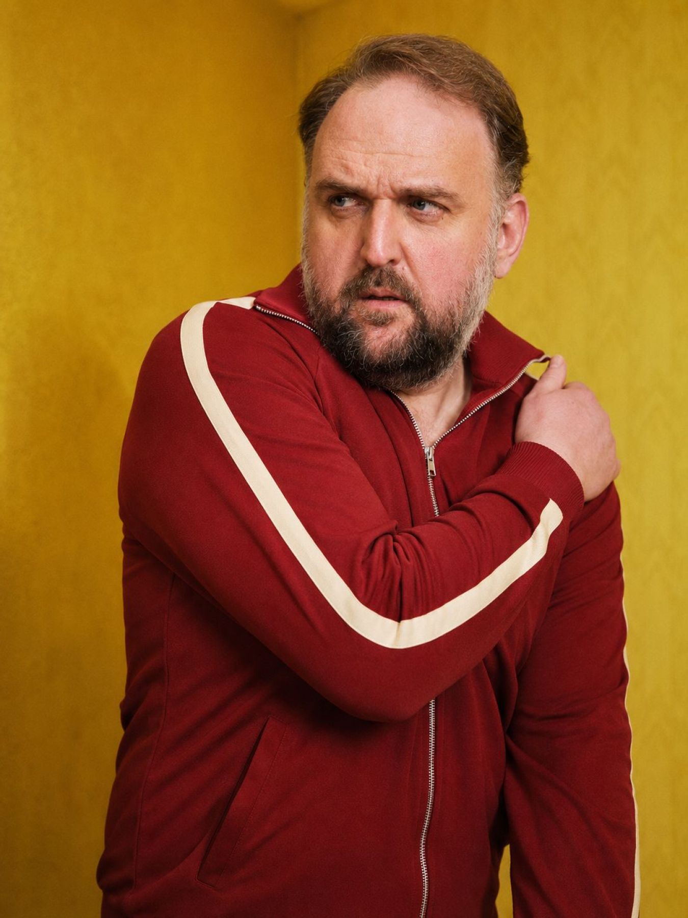 Ronny Schuster in roter Trainingsjacke mit weißen Streifen und skeptischem Blick.